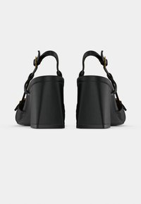 Sandales à talons hauts noires avec un talon épais, une bride de cheville ajustable et des accents tissés, présentant une finition en cuir lisse.