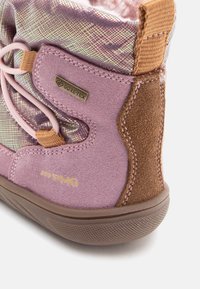 Közelkép egy rózsaszín és barna velúrból készült téli csizmáról, Gore-Tex felirattal, rózsaszín cipőfűzőkkel és barna gumitalppal.