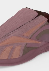 Κοντινό πλάνο ενός mauve και ροζ αθλητικού παπουτσιού με επενδύσεις από σουέτ και υφασμένη σόλα, που αναδεικνύει τα πλευρικά και επάνω υλικά και τις λεπτομέρειες του σχεδιασμού.