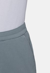 Close-up of a light blue elastic waistband on pants with visible stitching and a side pocket, worn with a white top.