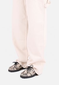 Black and beige snake-print shoes with textured upper, round toe, and black rubber sole, worn with oversized light-colored pants.