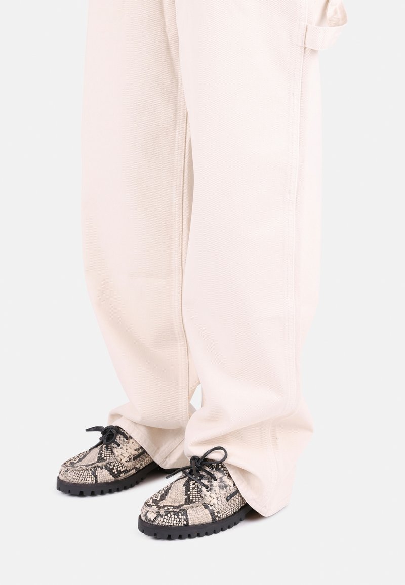 Black and beige snake-print shoes with textured upper, round toe, and black rubber sole, worn with oversized light-colored pants.