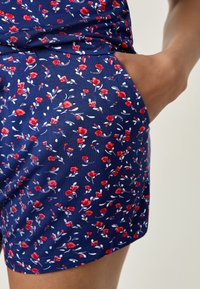 Tissu bleu marine avec un petit motif floral comportant des roses rouges et des feuilles vertes. Le short a une poche latérale et une texture lisse.