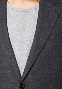 Szary z teksturą żakiet z klapami, zapinany na jeden guzik, z małym logo na klapie, nałożony na jasnoszary T-shirt.