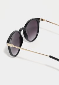 Black plastic cat-eye sunglasses with dark lenses. Gold metal accents on the temples and hinges. Smooth finish and angular shape.