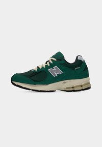 Πράσινο παπούτσι New Balance 2002R με λευκά κορδόνια, επάνω μέρος από δίχτυ και σουέντ, και κρεμ σόλα με μαύρη πέλμα, εμφανίζεται σε πλευρική προβολή.