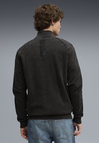 Mørkegrå sweatshirt med ribbet krave, struktureret stof og logomærke på bagsiden; parret med lyseblå jeans.