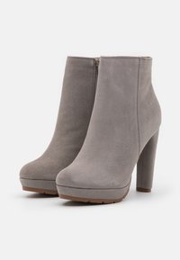 Un par de botines de tacón alto de ante gris con cremalleras laterales y suelas con plataforma sobre un fondo blanco.