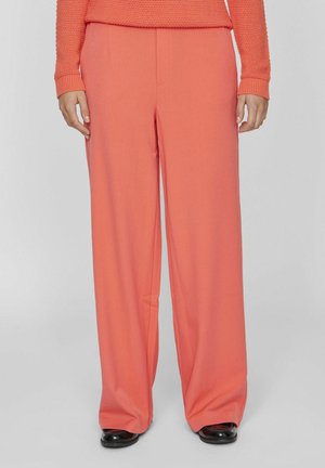 Pantalones de pierna ancha color coral con una textura suave y pliegues frontales, combinados con calzado negro. La tela es ligera y fluida.