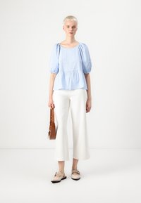 Blå og hvit rutete peplum-bluse med puffede ermer, kombinert med hvite vide bukser og beige leiligheter, accessorert med en brun crossover-veske.