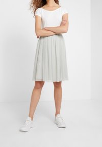 Gonna di tulle grigia chiara con design a strati e motivo a pois, abbinata a un top bianco aderente e sneakers bianche.