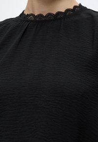 Gros plan d'un chemisier en tissu noir texturé avec un bord en dentelle noire festonné autour de l'encolure.