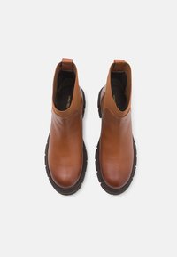 Paire de bottines en cuir marron avec semelles épaisses noires et panneaux latéraux élastiques, vue de dessus sur fond blanc.