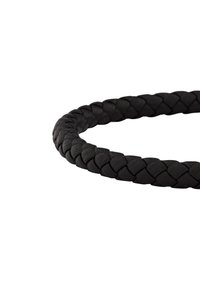 Primer plano de una pulsera de cuero trenzado negro formando un lazo sobre un fondo blanco.