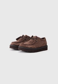 Sapatos de camurça castanhos com uma forma arredondada, apresentando um design com atacadores e uma sola de borracha espessa com padrões de aderência.
