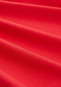 Heldere rode stof met een gladde textuur, voorzien van een subtiele glans en zachte plooien. Het materiaal lijkt zacht en lichtgewicht.