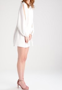 Bíl dress s dlouhými balónovými rukávy a odhalenými rameny, s tkaničkami na zápěstí. V kombinaci se světle růžovými sandály na podpatku.