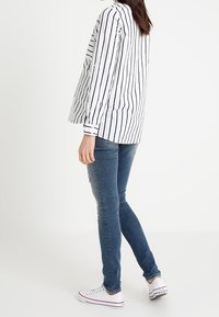 Camisa de rayas de manga larga en blanco y azul marino, combinada con jeans ajustados azules y zapatillas blancas. Ajuste casual con puños abotonados y dobladillo recto.