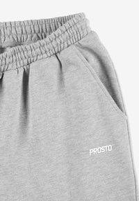 Szare dresy wykonane z miękkiego materiału z elastycznym pasem. Posiadają boczne kieszenie oraz biały logo "PROSTO" na dolnej części nogawki.