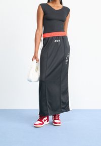 Svart sportmaxikjol med elastisk röd midja, vita sidostrepen och Nike-logotyp. Matchad med en åtsittande svart topp och röda sneakers.