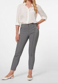 Pantalons à carreaux noir et blanc avec une coupe cintrée, taille haute et poches latérales, associés à un chemisier blanc et des talons blancs.