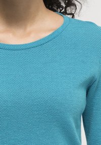 Teal textured sweater with a round neckline, featuring a honeycomb pattern and long sleeves. Smooth fabric with a slight sheen.