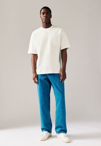 Hellgraues T-Shirt mit kurzen Ärmeln und Brusttasche, kombiniert mit hoch taillierter blauer Jeans und weißen Sneakers. Schlichtes Design, entspannte Passform.