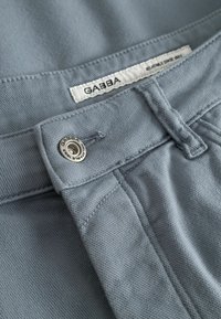 Ανοιχτό μπλε παντελόνια Gabba με κουμπί και ετικέτα που δείχνει το όνομα της μάρκας και "Relaxed since 1989."