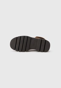 Suela de bota de gamuza marrón, con una superficie de goma texturizada y ranuras horizontales, diseñada para ofrecer agarre y durabilidad.