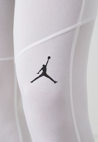 Biele športové legíny so štíhlym strihom, s čiernym logom Jumpman a jemným detailom švov pre štýlový vzhľad.