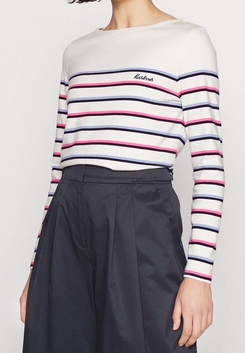 Weißes Langarmoberteil mit horizontalen schwarzen, blauen und pinken Streifen; runder Halsausschnitt; gesticktes Logo auf der linken Brust. Kombiniert mit einem dunklen Rock.