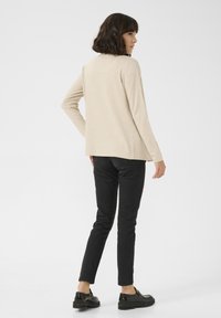Beige langhandschut met een ontspannen fit, gecombineerd met zwarte slim-fit broeken en zwarte schoenen. Happige textuur, eenvoudig ontwerp, geen patronen.