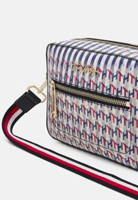 Gennemsigtig PVC-taske med et geometrisk mønster i blå, rød og creme, med en guldfarvet lynlås og en justerbar multistribet rem.