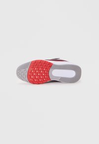Semelle de chaussure de sport rouge et grise avec caoutchouc texturé pour l'adhérence, présentant un motif de semelle et une section de talon blanche lisse.