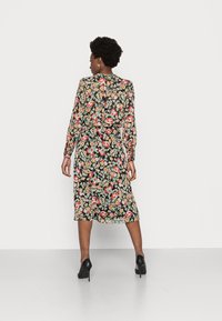 Vestido preto fluido com padrão floral colorido, mangas longas, cintura ajustada e barra abaixo do joelho. Sapatos de salto pretos.