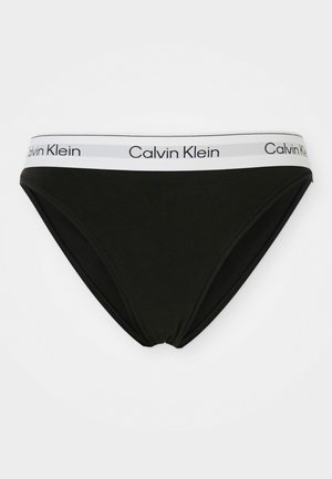 Zwarte katoenen bikini slip met een witte elastische tailleband waarop "Calvin Klein" in het zwart is gedrukt. Glad profiel, laag uitgesneden ontwerp.