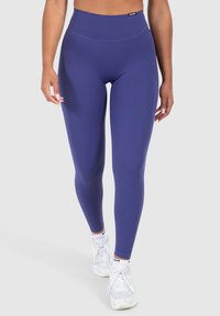 Leggings viola a vita alta realizzati in tessuto elasticizzato, con una texture liscia e un'etichetta del logo in vita. Abbinati a sneakers bianche.