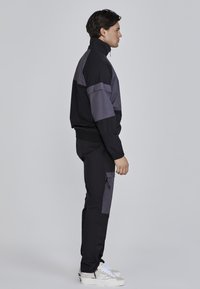 Sports tracksuit i sort og grå, zip-up jakke med høj krave, elastiske manchetter og matchende bukser med cargo-lomme detaljer.