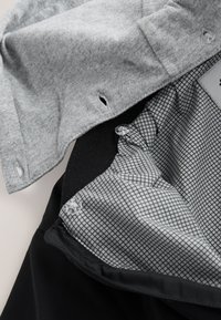 Col chemise en tissu gris sur une veste noire avec une doublure grise à carreaux, dotée de fermetures par boutons et d'ouvertures de col ventilées.