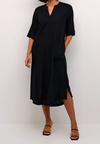Vestido negro hasta la rodilla con escote en V, mangas 3/4, bolsillo lateral y aberturas laterales, hecho de una tela suave y ligera.