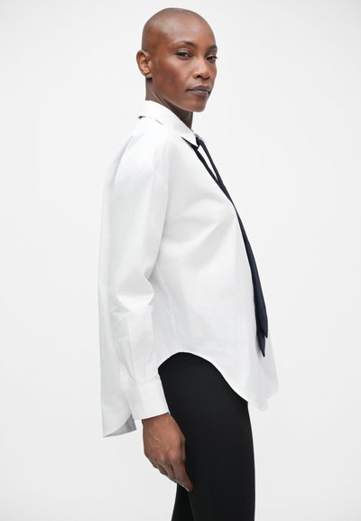 Witte button-up shirt met een puntige kraag, lange mouwen en een afgeronde zoom. Draag met een donkere stropdas en zwarte slim-fit leggings. Glad textuur.