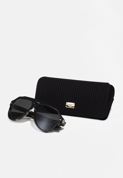 Ochelari de soare negri cu un design geometric, lentile închise și brațe din scoică de țestoasă maro cu model. Include o carcasă texturată neagră cu accente aurii.