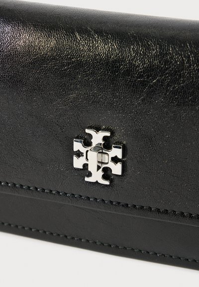 Κοντινό πλάνο από μαύρο δερμάτινο πορτοφόλι με ασημένια μεταλλική αγκράφα σε σχήμα σταυρού και λεπτομερή ραφή κατά μήκος των άκρων.