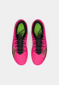 Bright pink athletic shoes with black laces, textured surface, and a green insole. Features a yellow accent stripe on the side.