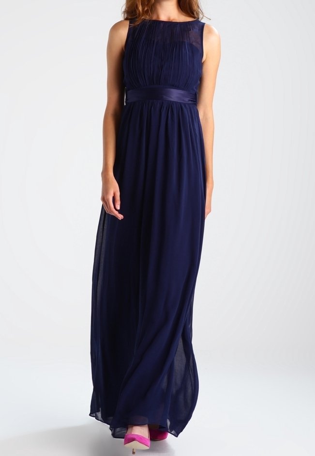Abito maxi blu navy in tessuto leggero, con busto plissettato, scollatura trasparente e cintura in satin. Il modello indossa tacchi rosa.