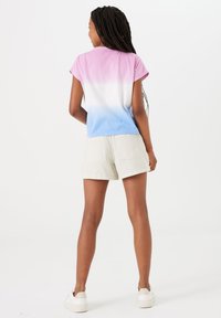 Korte mouw t-shirt met een roze-blauwe gradient ontwerp, gecombineerd met lichtbeige shorts. Het shirt heeft een ronde halslijn en een relaxte pasvorm.