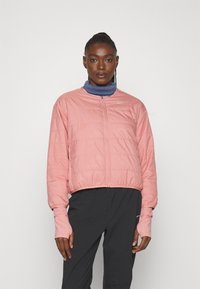 Veste doudoune rose avec une fermeture éclair à l'avant, des poignets côtelés et un design court. Superposée à un top à col montant bleu. Tissu léger, texture lisse.