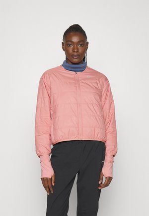 Roze pufferjas met een rits aan de voorkant, ribgebreide manchetten en een cropped design. Gelaagd over een blauwe trui met een hoge kraag. Lichtgewicht stof, gladde textuur.