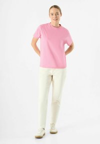 Korte mouw roze katoenen t-shirt, ronde halslijn, gecombineerd met lichtbeige broek en witte sneakers met beige accenten. Eenvoudig ontwerp, gladde textuur.