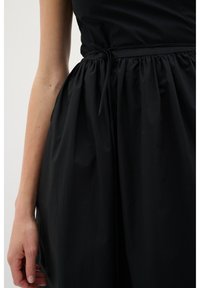 Schwarzes Kleid mit einem taillierten Oberteil und einem gerafften, fließenden Rock. Die Taille ist mit einem passenden Band betont. Glattes Textilgewebe.